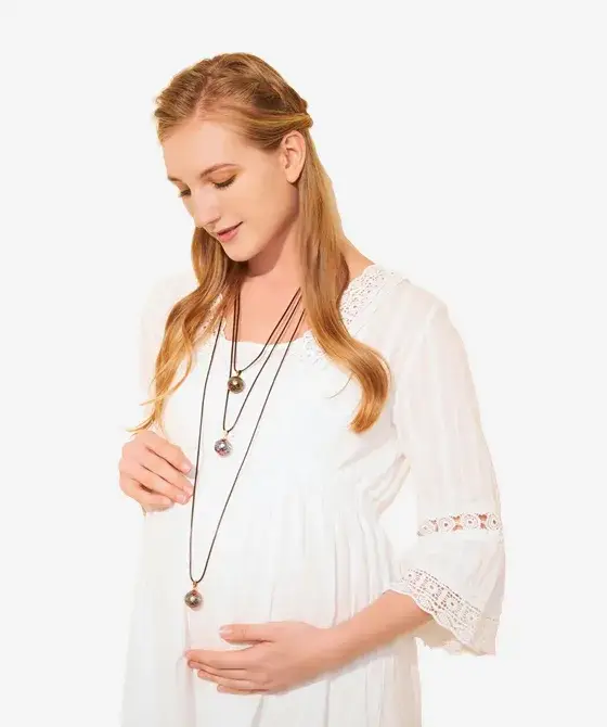 Une future maman en robe blanche porte deux bolas sur de longues chaînes, au niveau du ventre